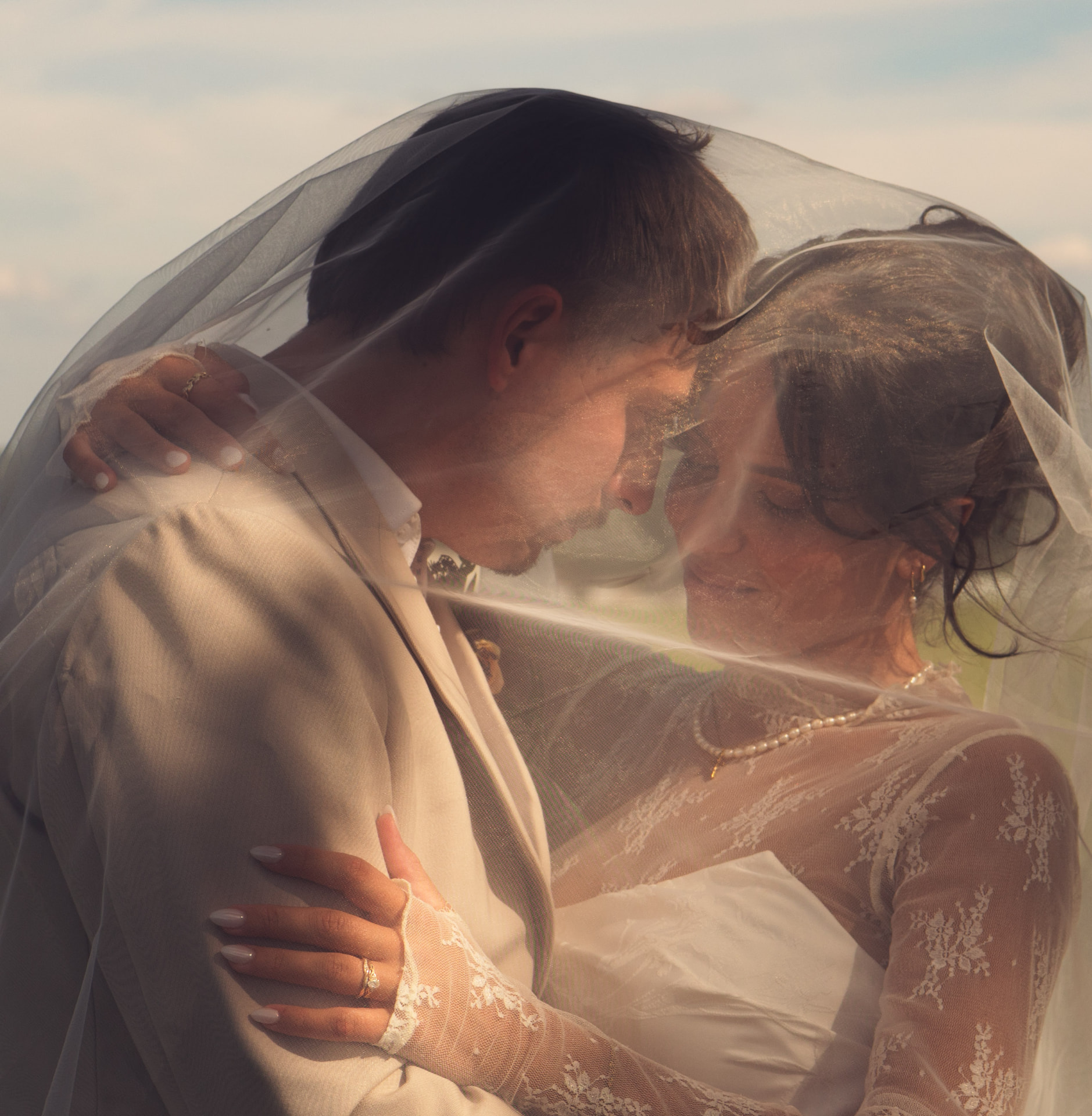 A couple forehead to forehead beneath a sheer veil at sunset